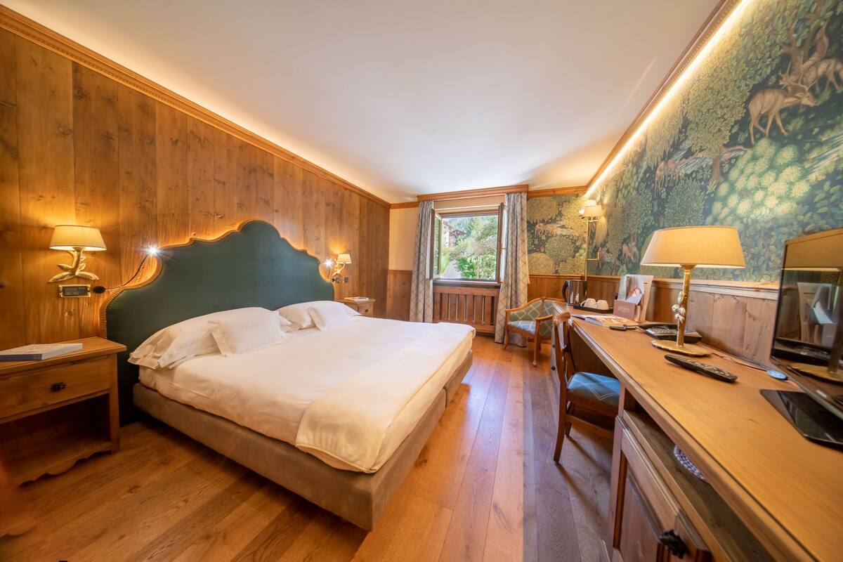 A hotel room with a large bed, wooden walls, a desk with a chair, and a mural on the wall.