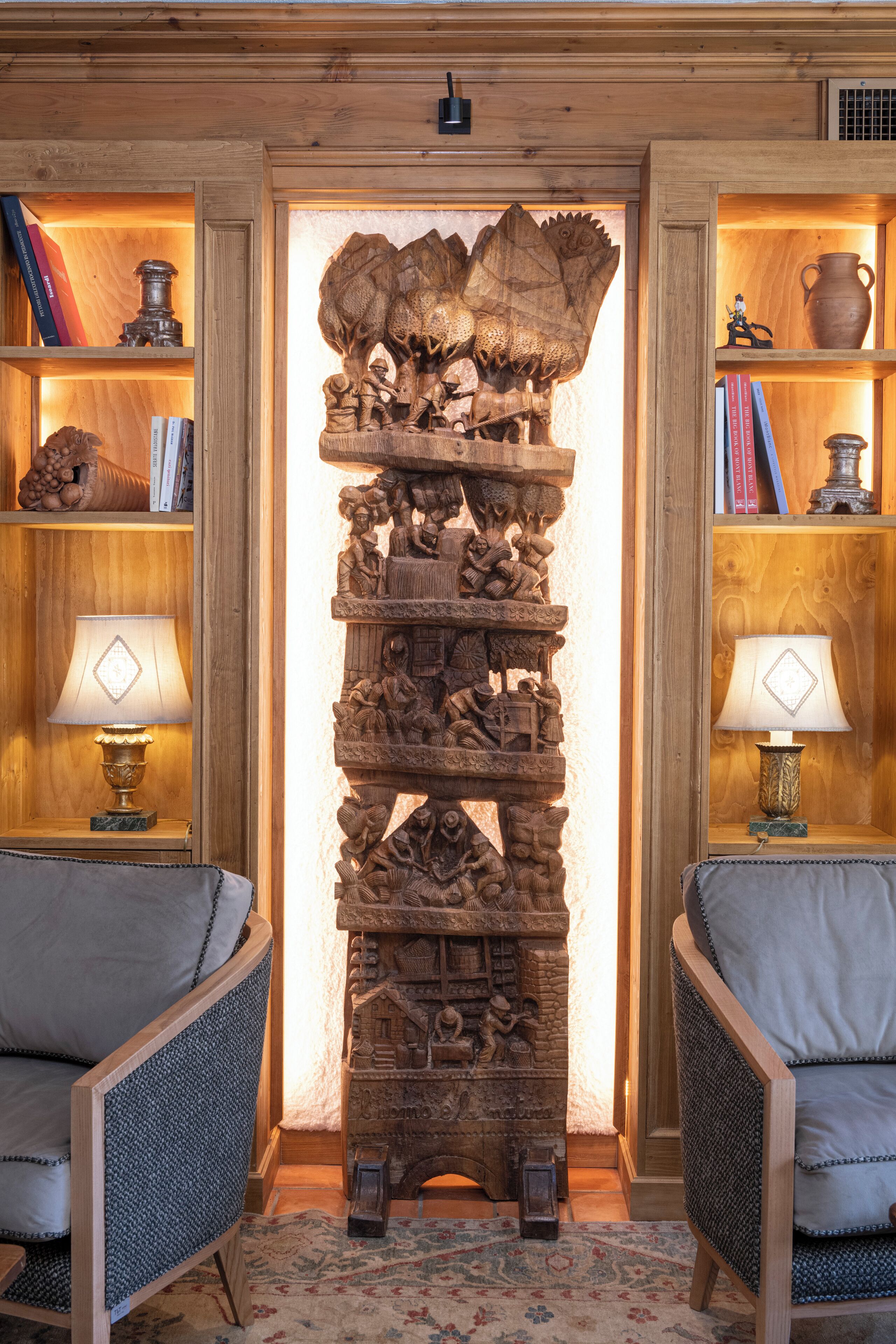 A room with a central wooden sculpture, two armchairs, and shelves with books and decorative items.
