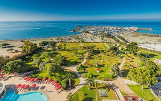 An aerial view of a resort with a swimming pool, sun loungers, and a marina.