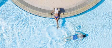 An aerial view of a swimming pool with two people in the water, surrounded by a tiled deck.