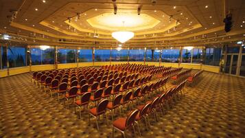 A large hall with rows of chairs and a view of the city through large windows.