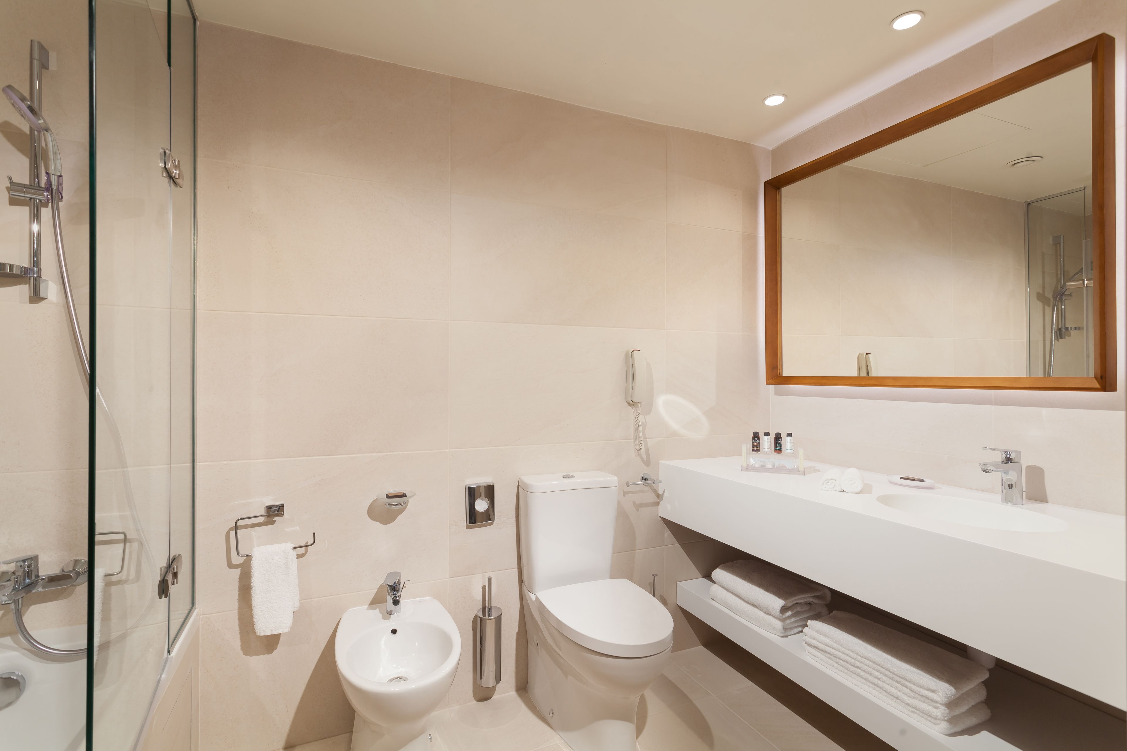 A modern bathroom with a glass shower enclosure, a bidet, a toilet, and a vanity with a mirror.