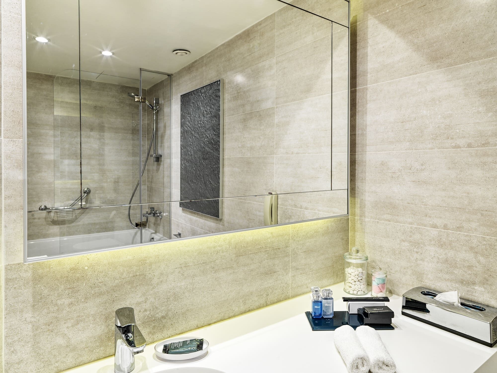 A modern bathroom with a glass shower enclosure, a large mirror, and a vanity with toiletries.