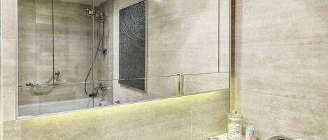 A modern bathroom with a glass shower enclosure, a large mirror, and a vanity with toiletries.
