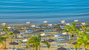 Una spiaggia con file di lettini e ombrelloni di paglia, palme e l'oceano.