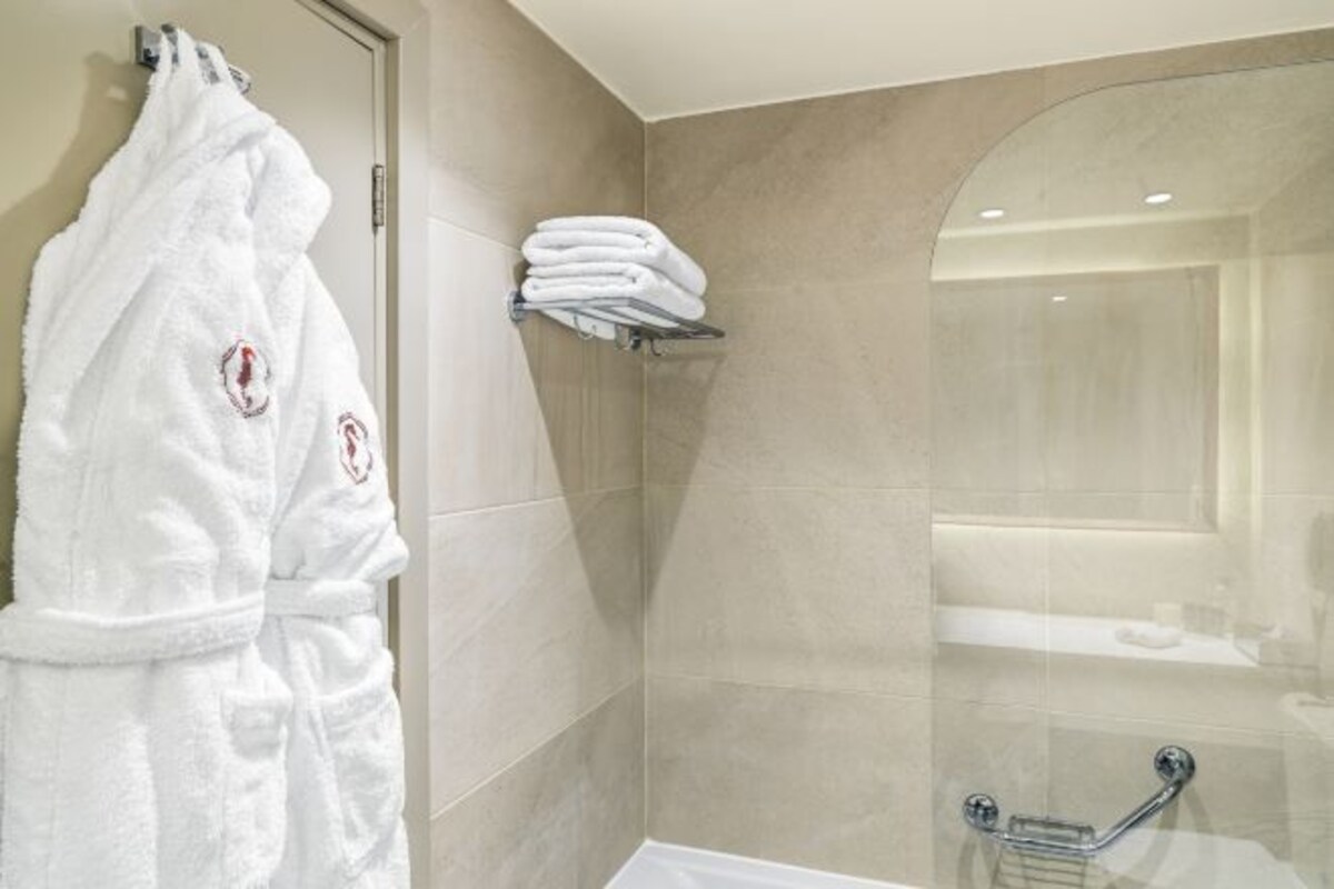 A bathroom with a glass shower enclosure, a white towel rack, and a white robe with a heart emblem.
