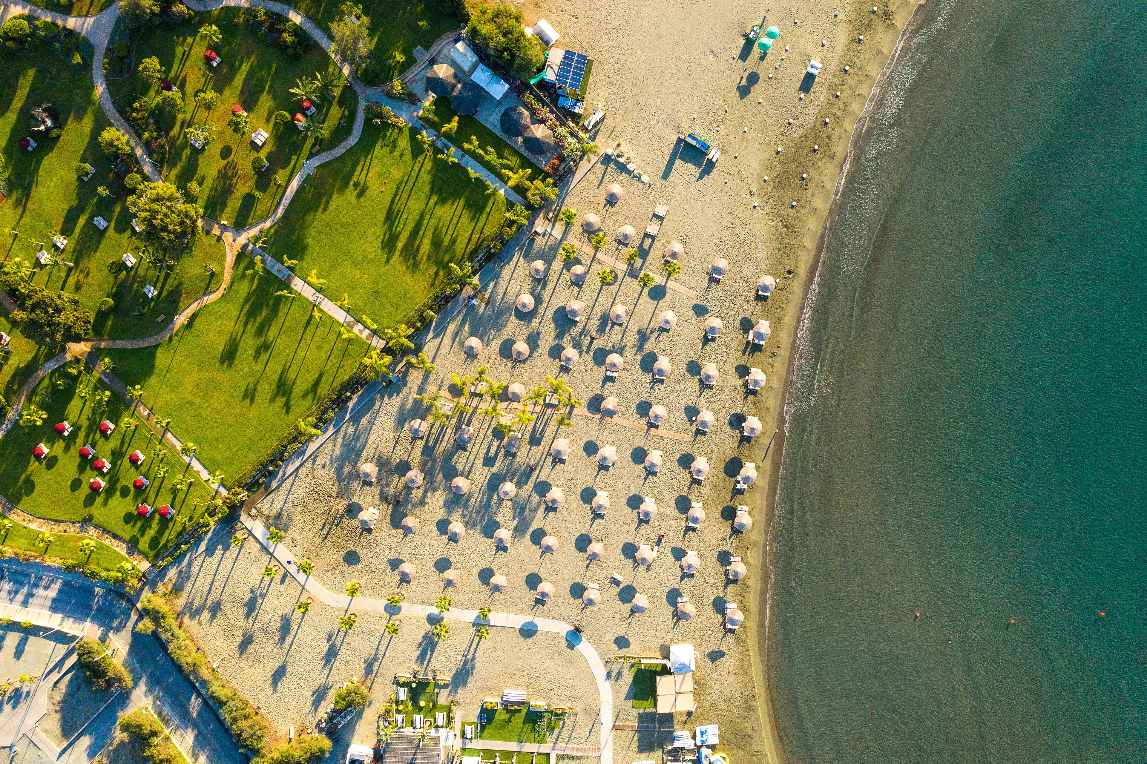 An aerial view of a beach resort with rows of umbrellas, a pool area, and a beachfront path.