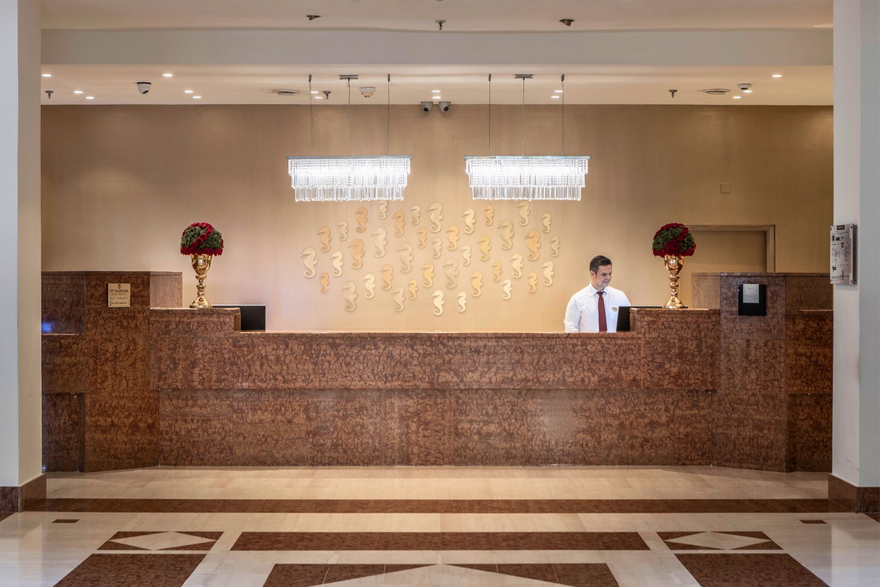 A reception desk with a marble counter, two chandeliers, and a receptionist.
