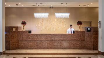 A reception desk with a marble counter, two chandeliers, and a receptionist.