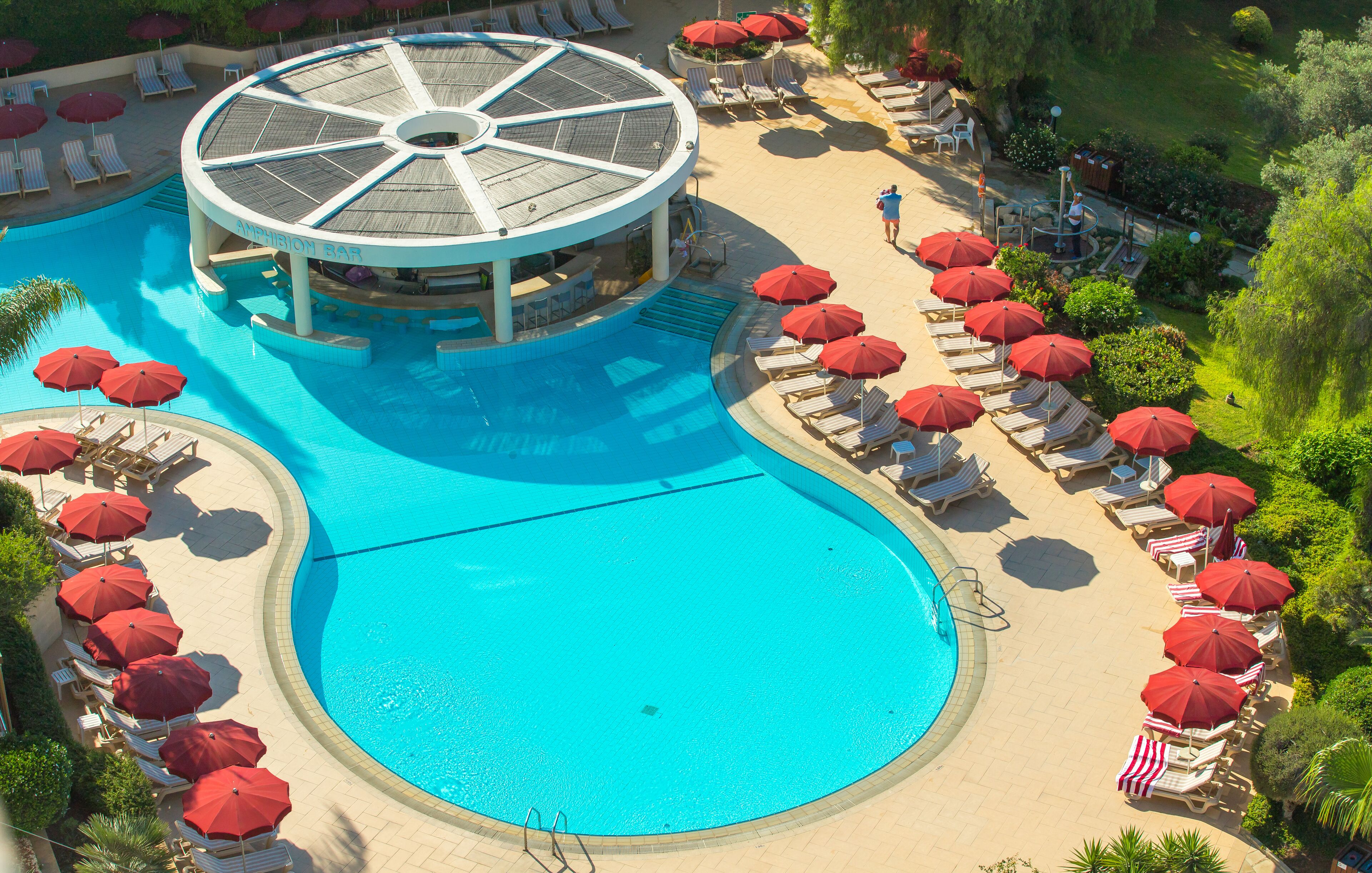 A large pool with a circular bar, sun loungers, and red umbrellas.