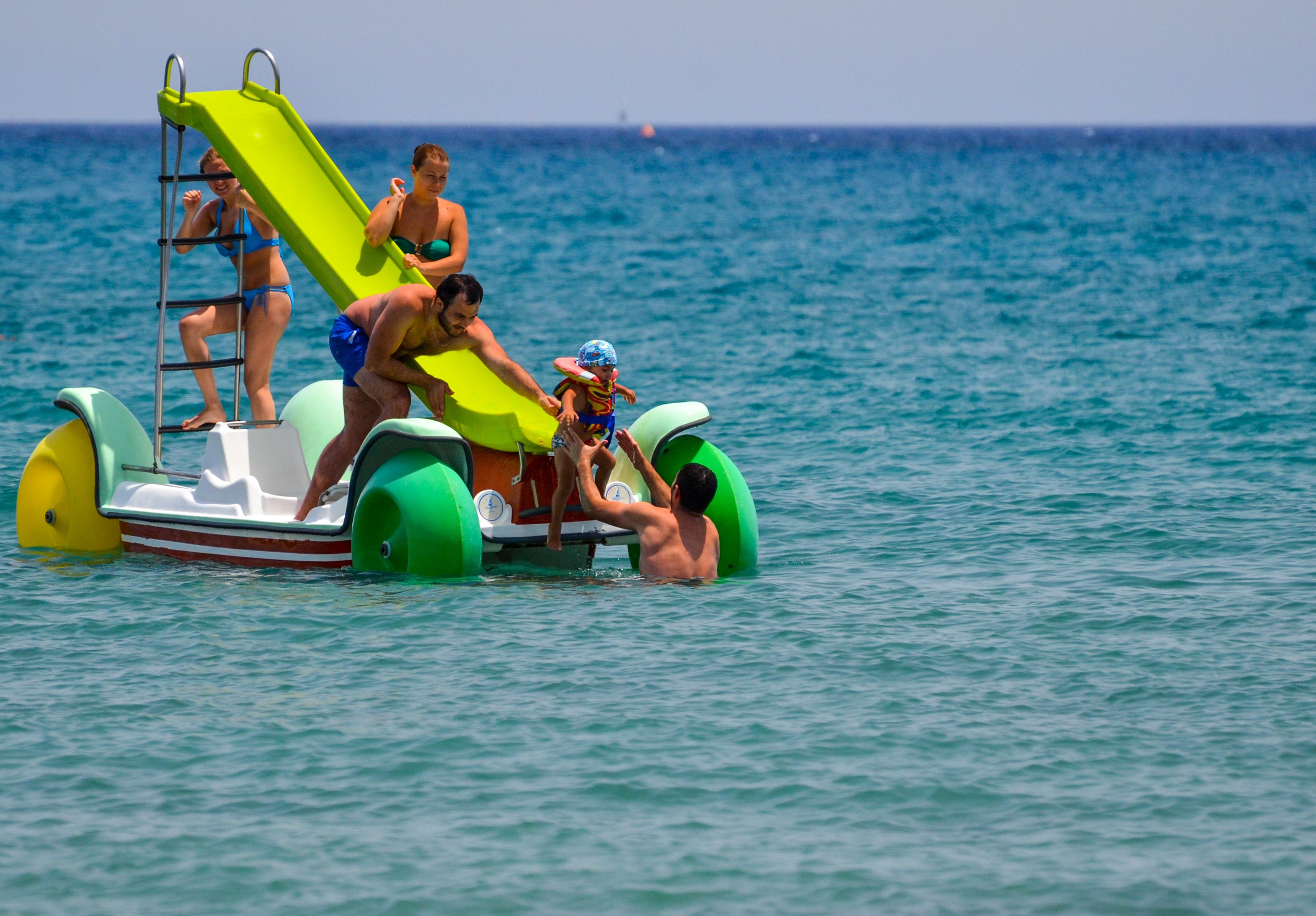 A watercraft with a green slide and a ladder, equipped with flotation devices.