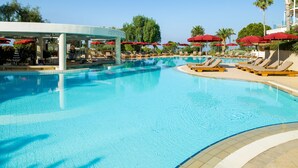 Una piscina con lettini e ombrelloni rossi, circondata da palme e un cielo sereno.