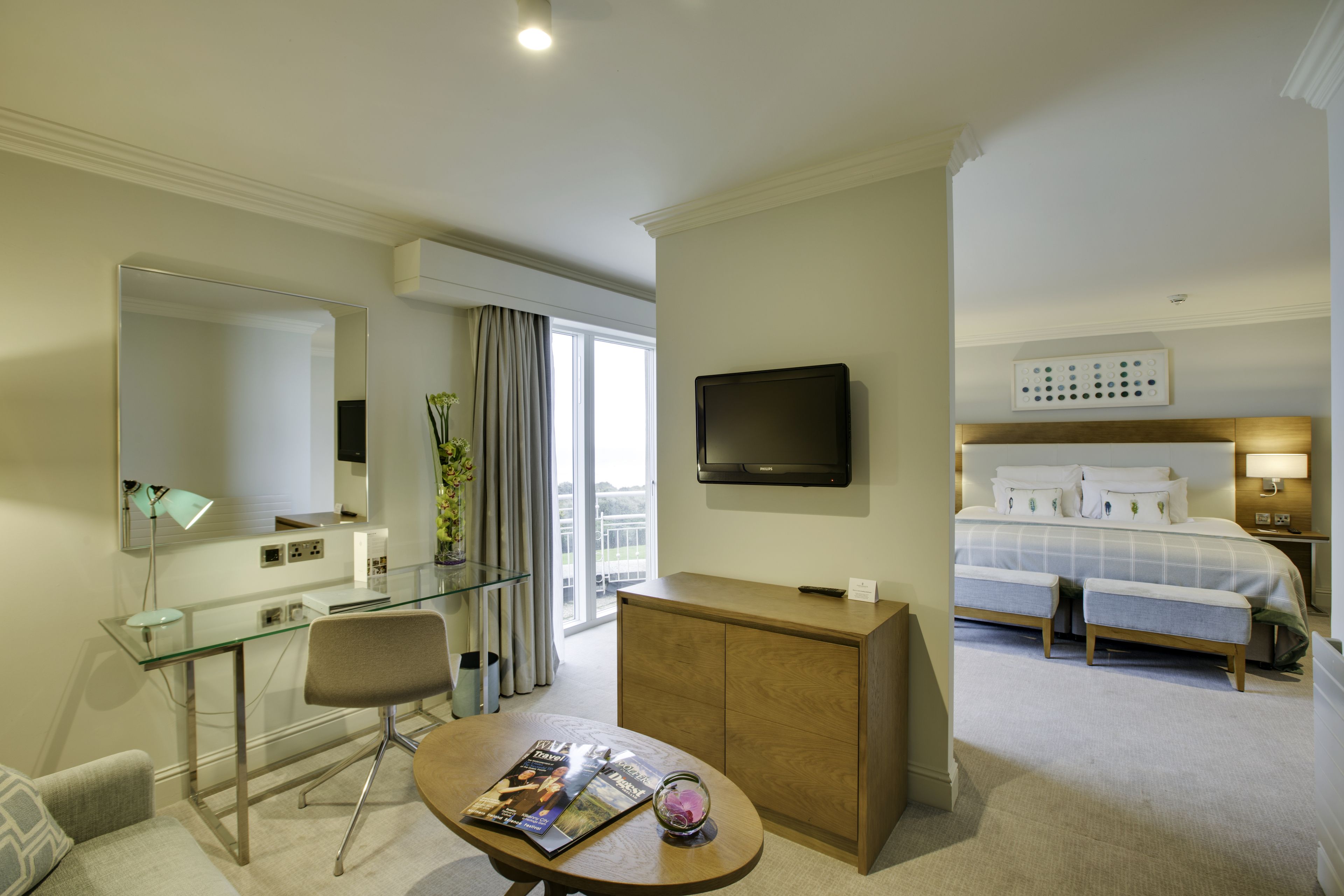 Een hotelkamer met een bed, een bureau met stoel, een televisie en een glazen tafel met tijdschriften.