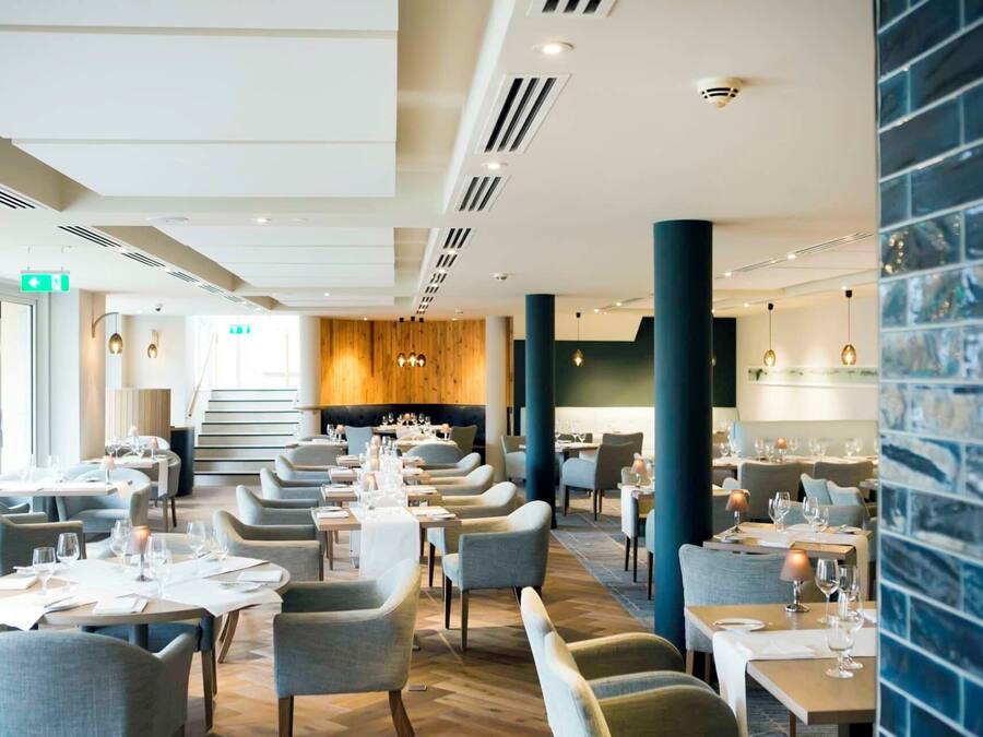 A modern restaurant with multiple dining areas, wooden flooring, and a staircase leading to an upper level.