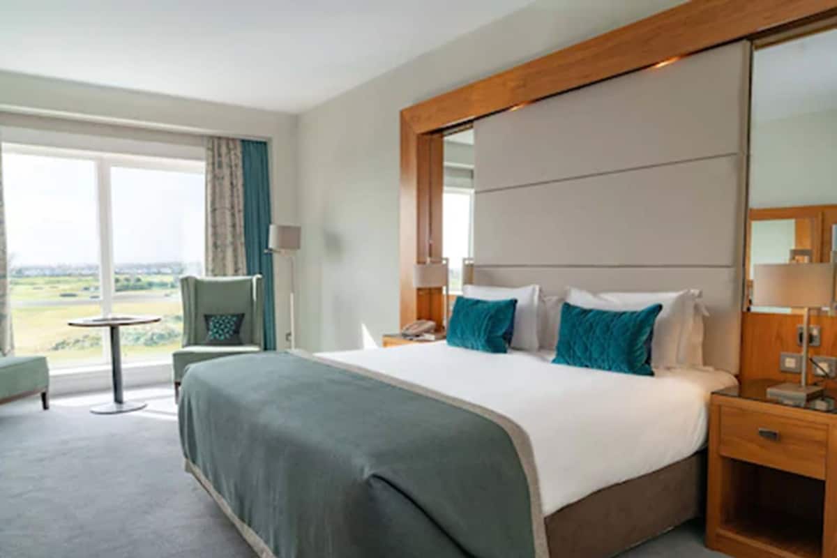 A hotel room with a large bed, a desk, a chair, and a view of the outdoors.