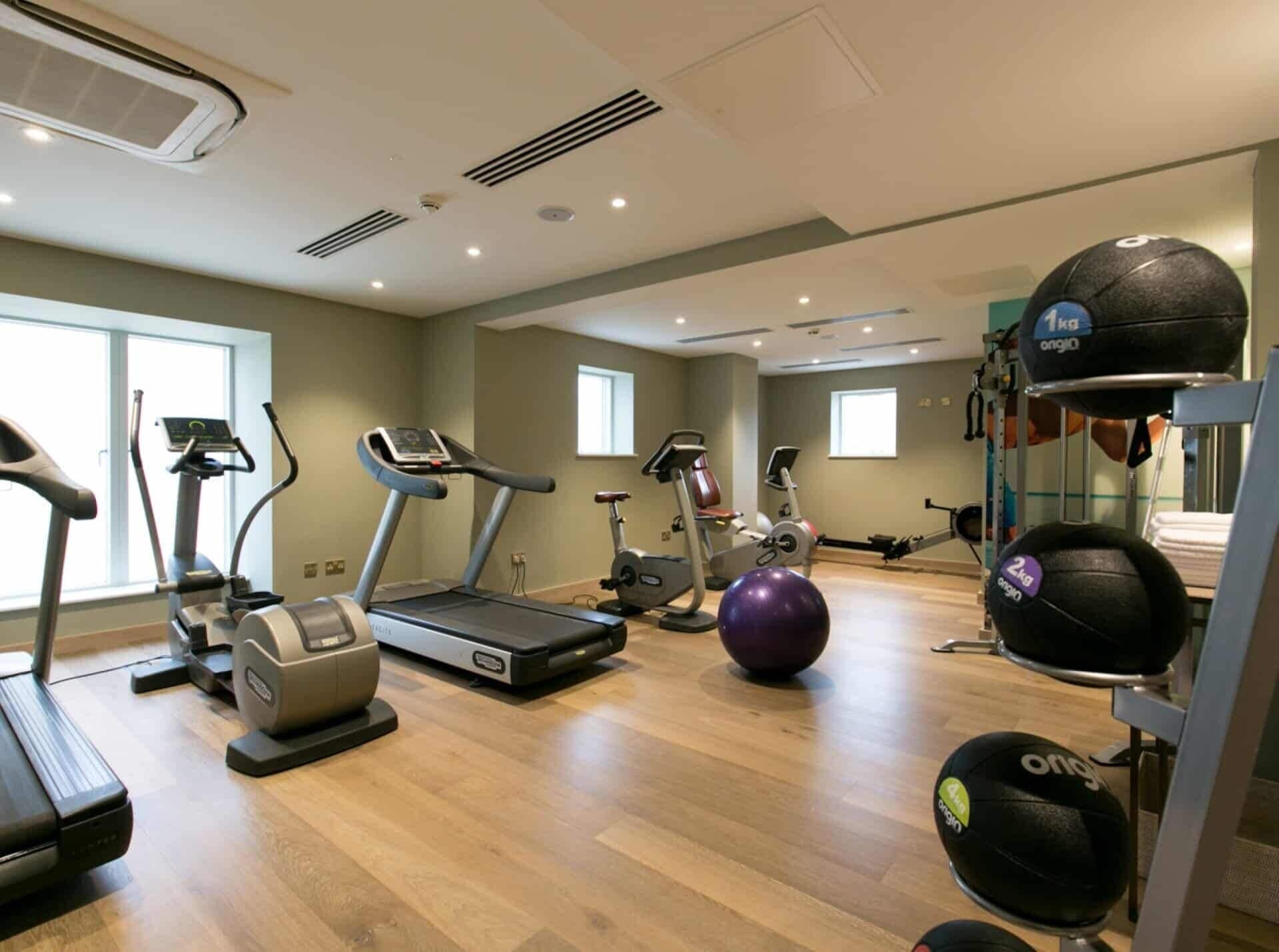 A gym with treadmills, elliptical machines, and a weightlifting area with exercise balls and dumbbells.