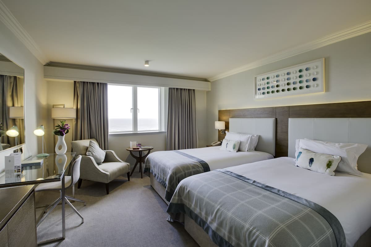 A hotel room with two beds, a desk, a chair, a small table, and a window with curtains.