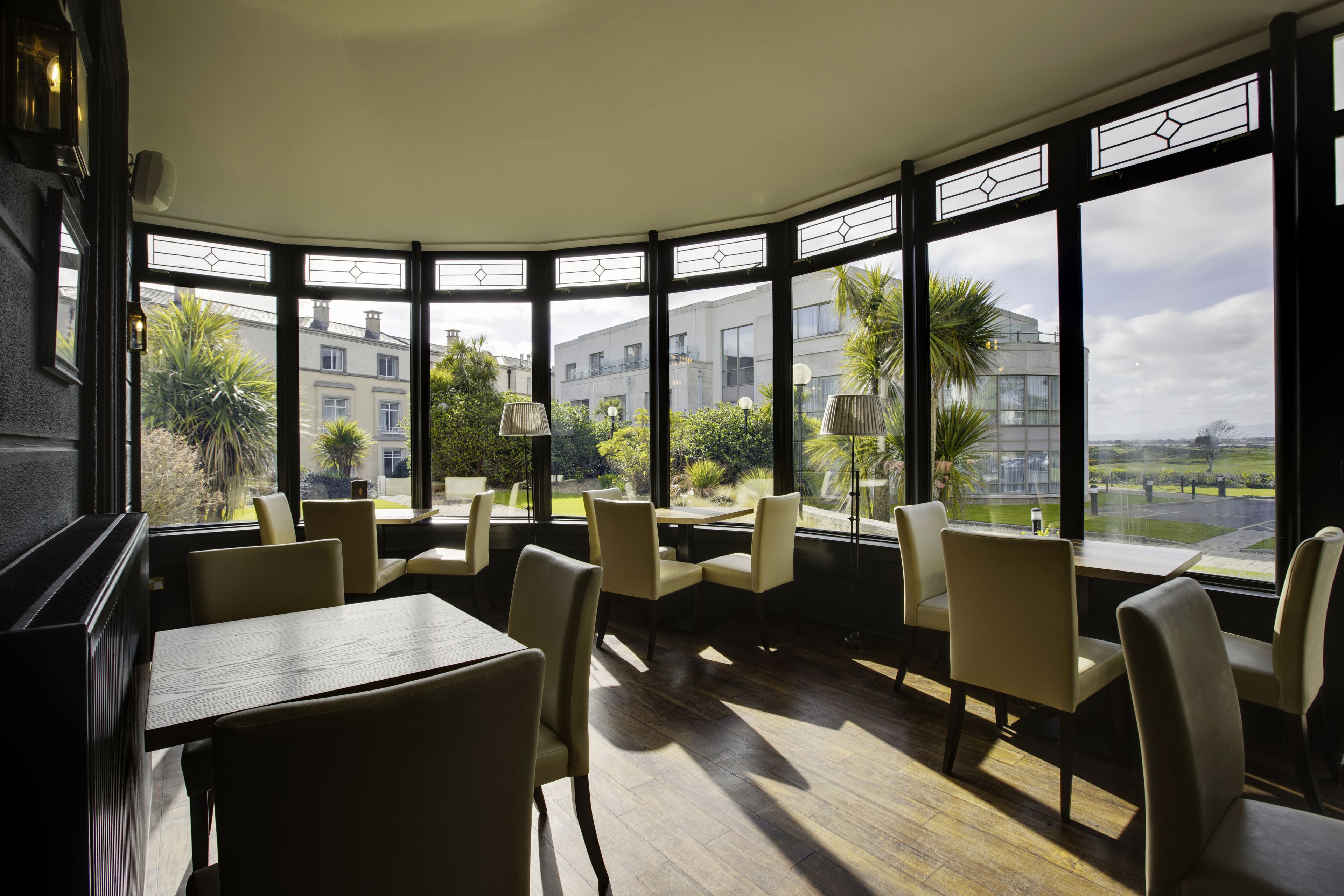 A restaurant with a curved bay window, wooden tables, and beige chairs.
