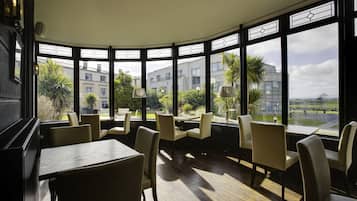 A restaurant with a curved bay window, wooden tables, and beige chairs.