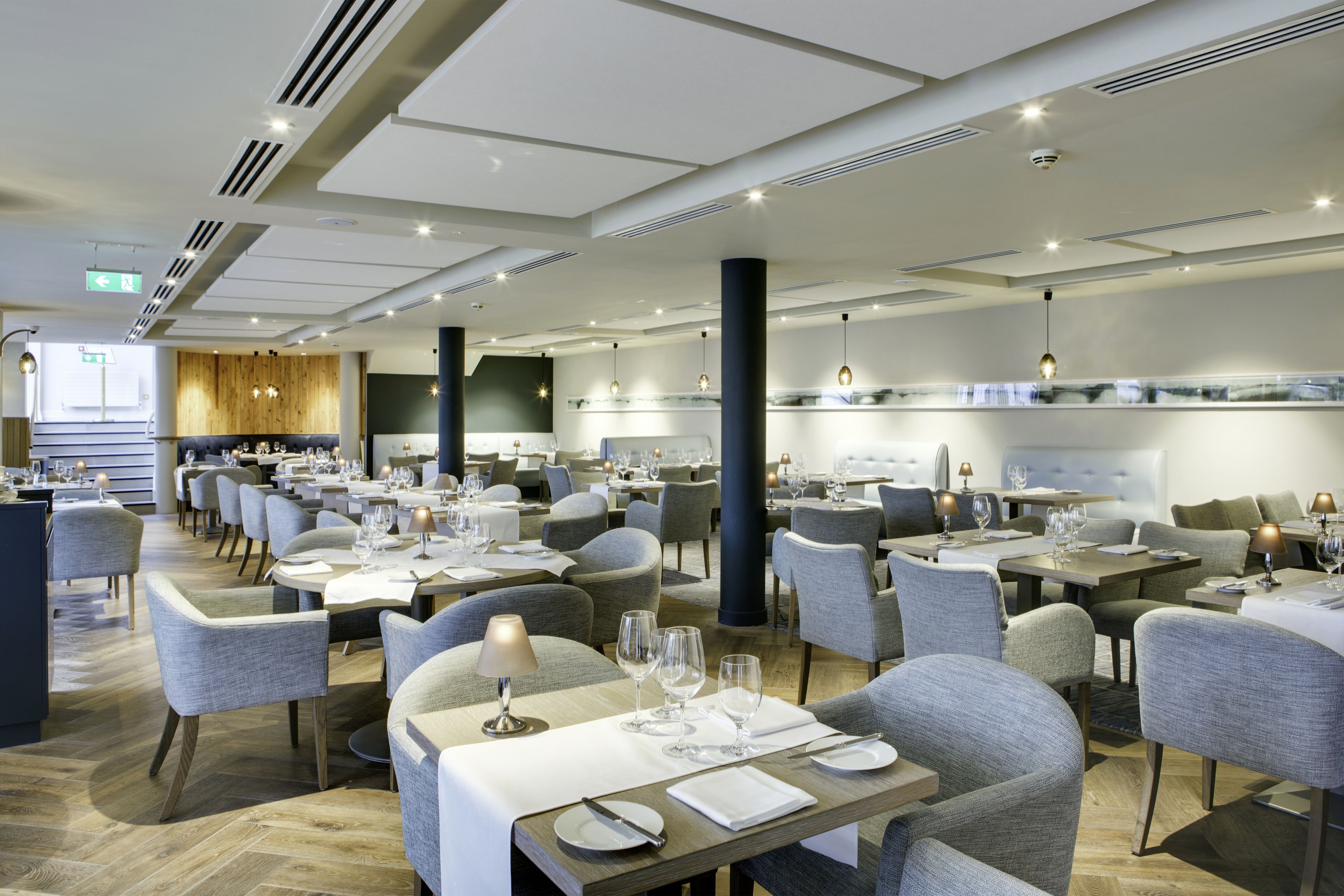 A spacious restaurant with multiple dining tables and chairs, a modern ceiling design, and a view of the cityscape through large windows.