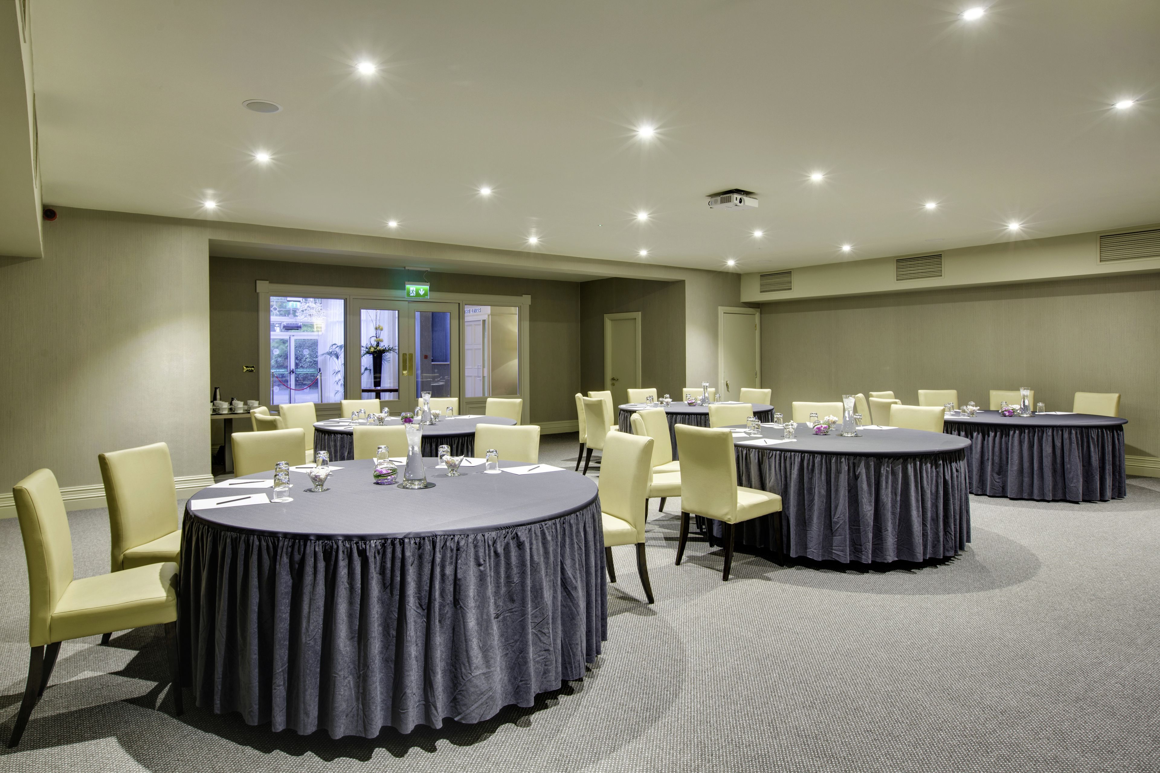 Un salón de conferencias con mesas redondas, sillas y un proyector.