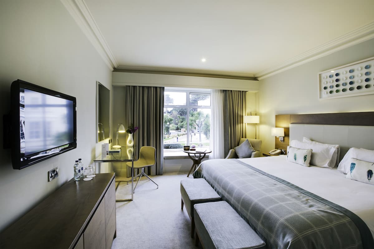 A hotel room with a large bed, a desk with a chair, a television, and a window with curtains.