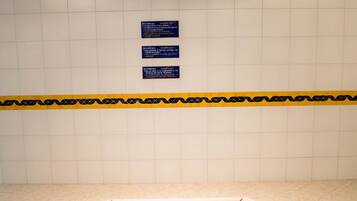 Un jacuzzi en una habitación con paredes de azulejos y techo azul. Hay carteles en la pared y un borde amarillo y negro cerca del suelo.