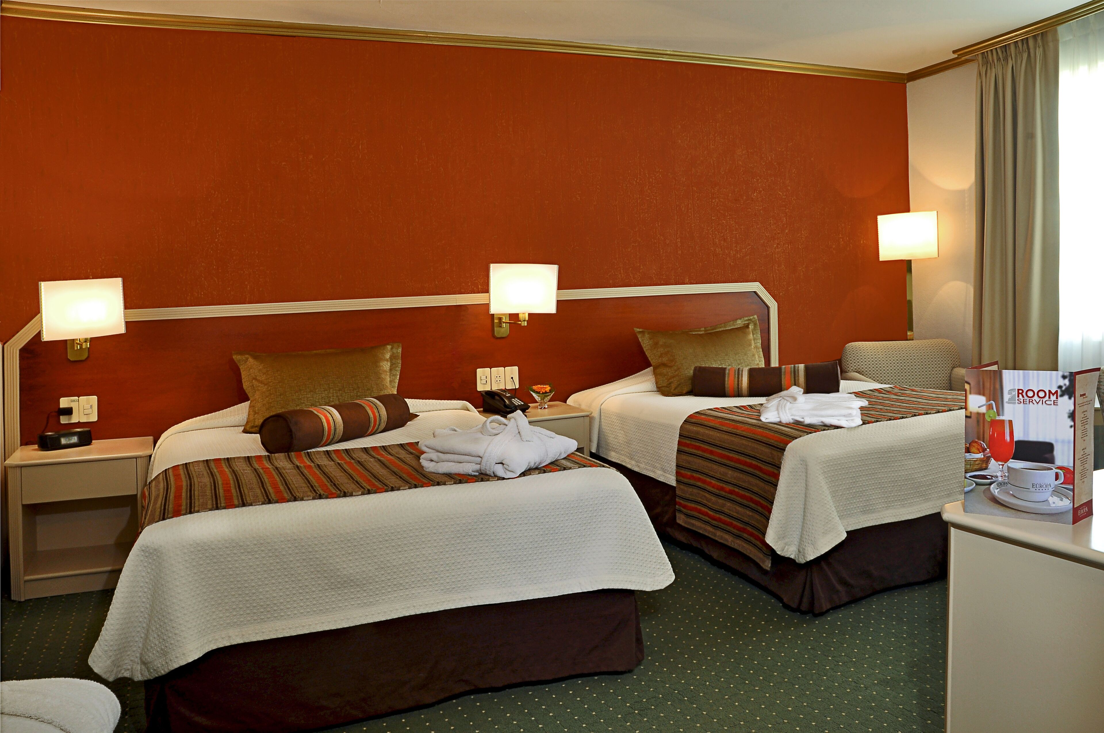 Een hotelkamer met twee bedden, elk met een kussen, een nachtkastje en een lamp.