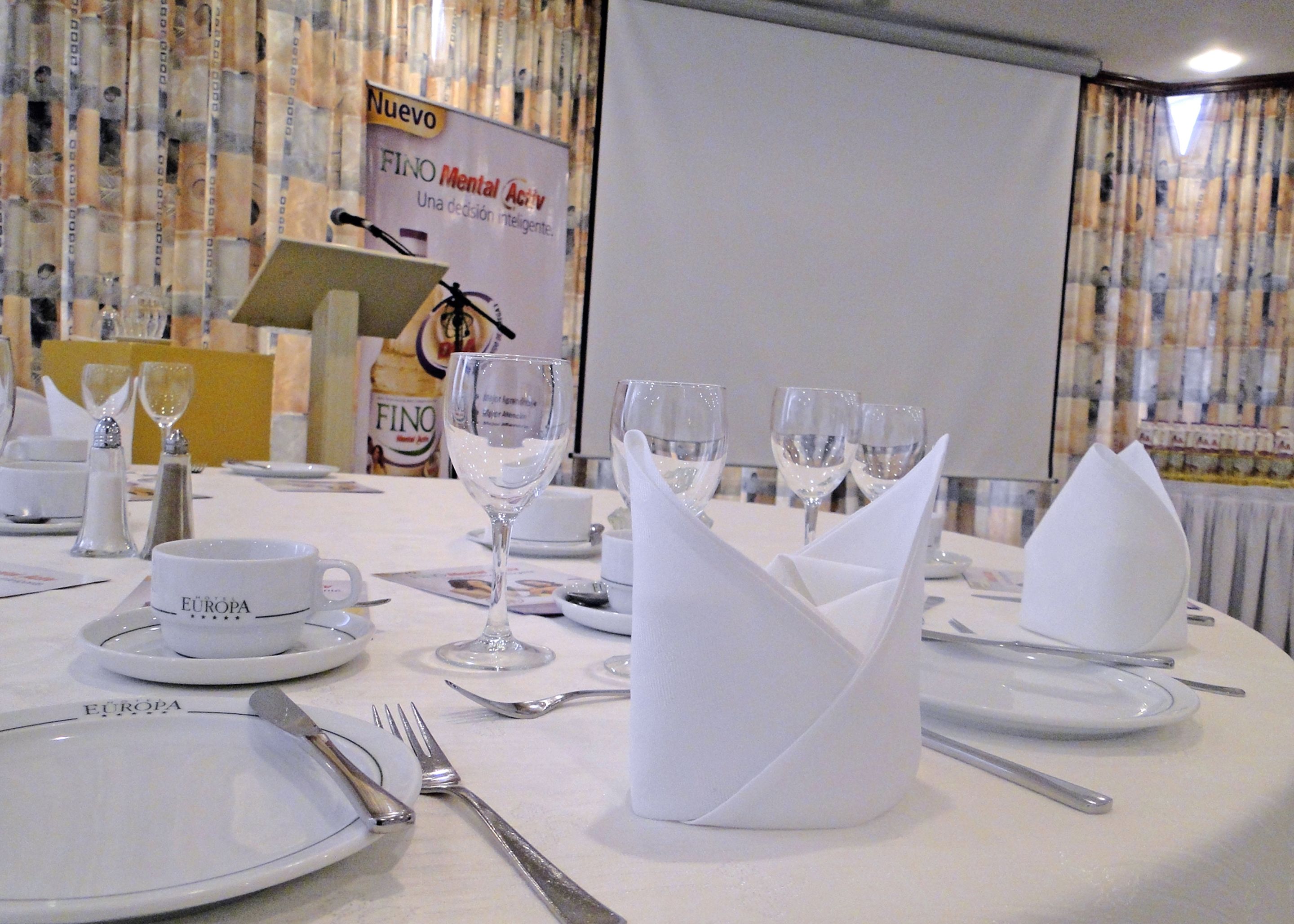 A conference room with a round table set for a meeting. There are nameplates, wine glasses, and a projector screen in the background.