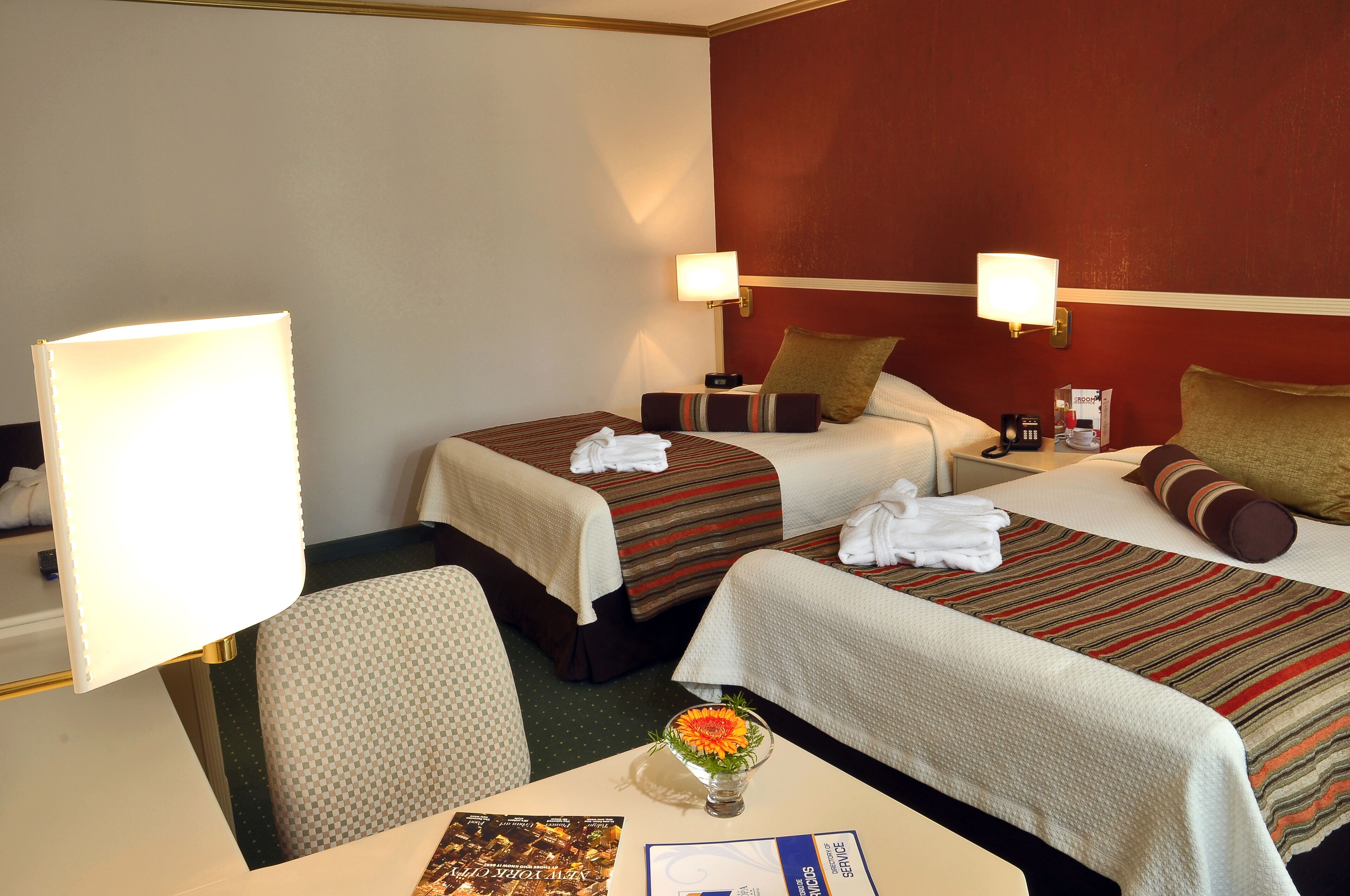 A hotel room with two beds, a table with a vase of flowers, and a chair.