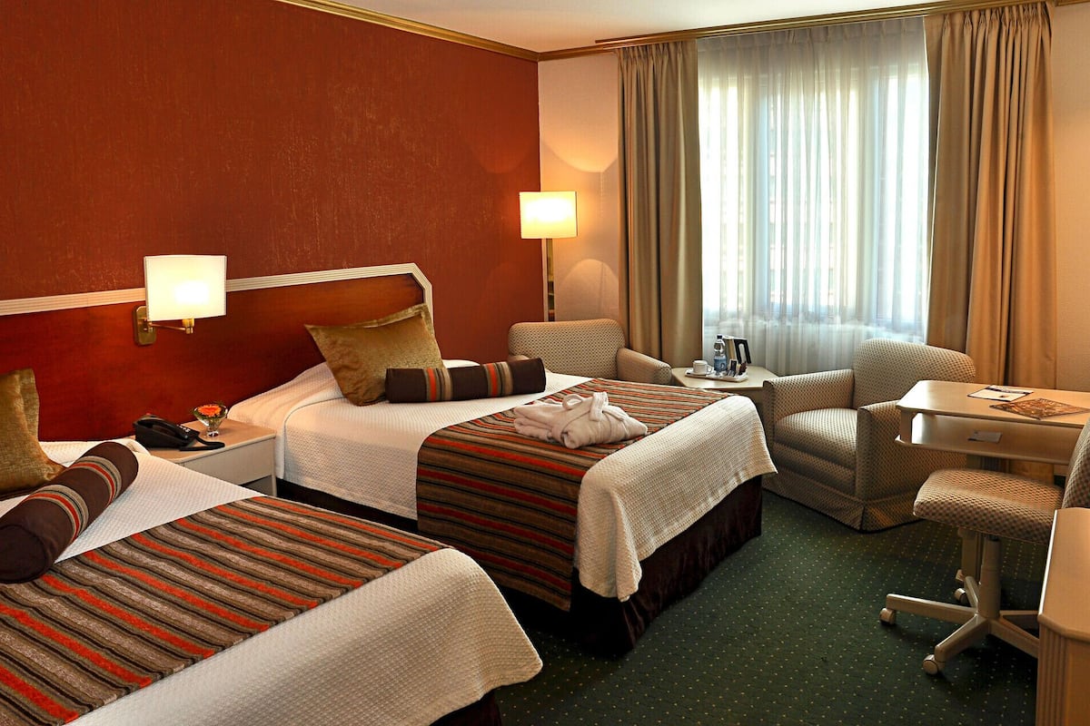 Habitación de hotel con dos camas, un escritorio, una silla y un ventanal con cortinas.