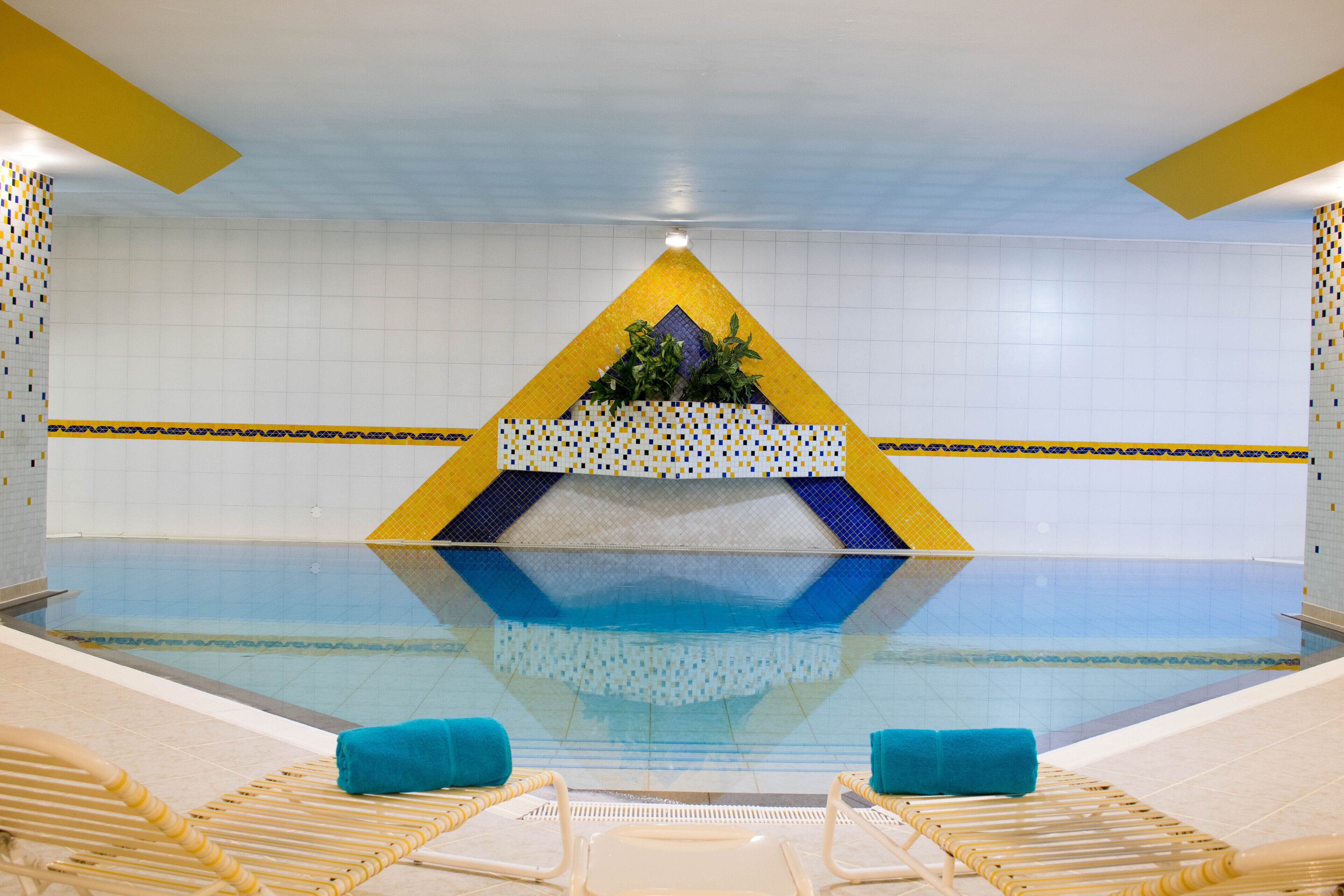 A swimming pool with a geometric design, two lounge chairs, and a tiled wall.