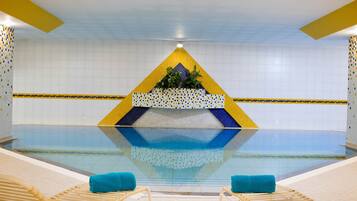A swimming pool with a geometric design, two lounge chairs, and a tiled wall.