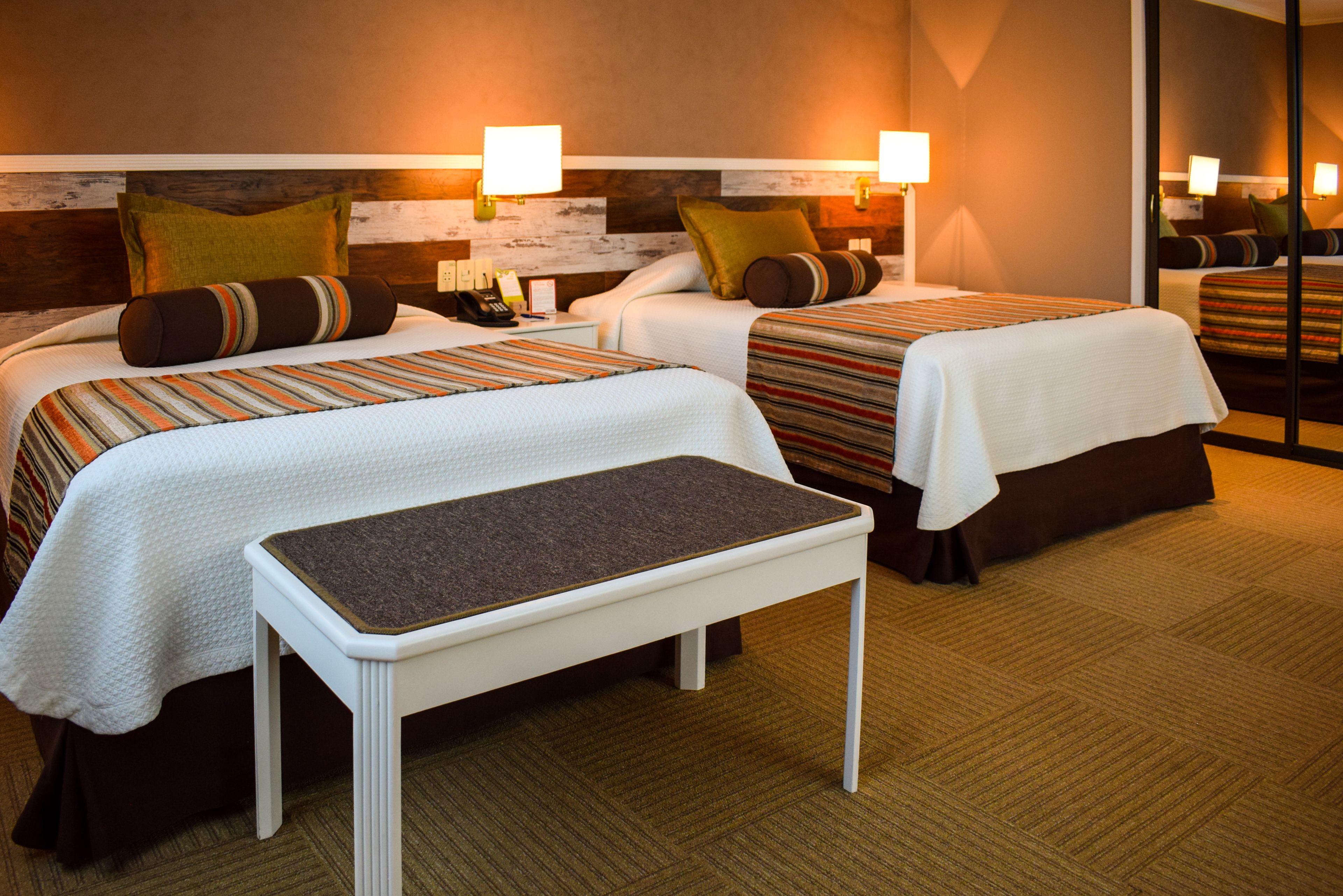 Habitación de hotel con dos camas, un banco y una mesita de noche con teléfono.