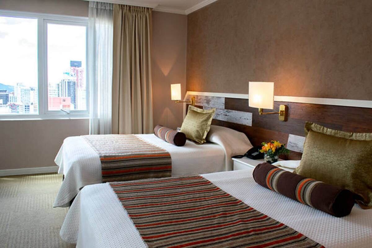 Habitación de hotel con dos camas, vista a la ciudad y diseño moderno.