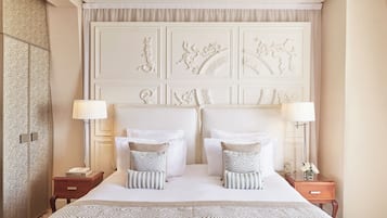 A hotel room with a large bed, two bedside tables, a headboard with decorative panels, and a nightstand with a lamp.
