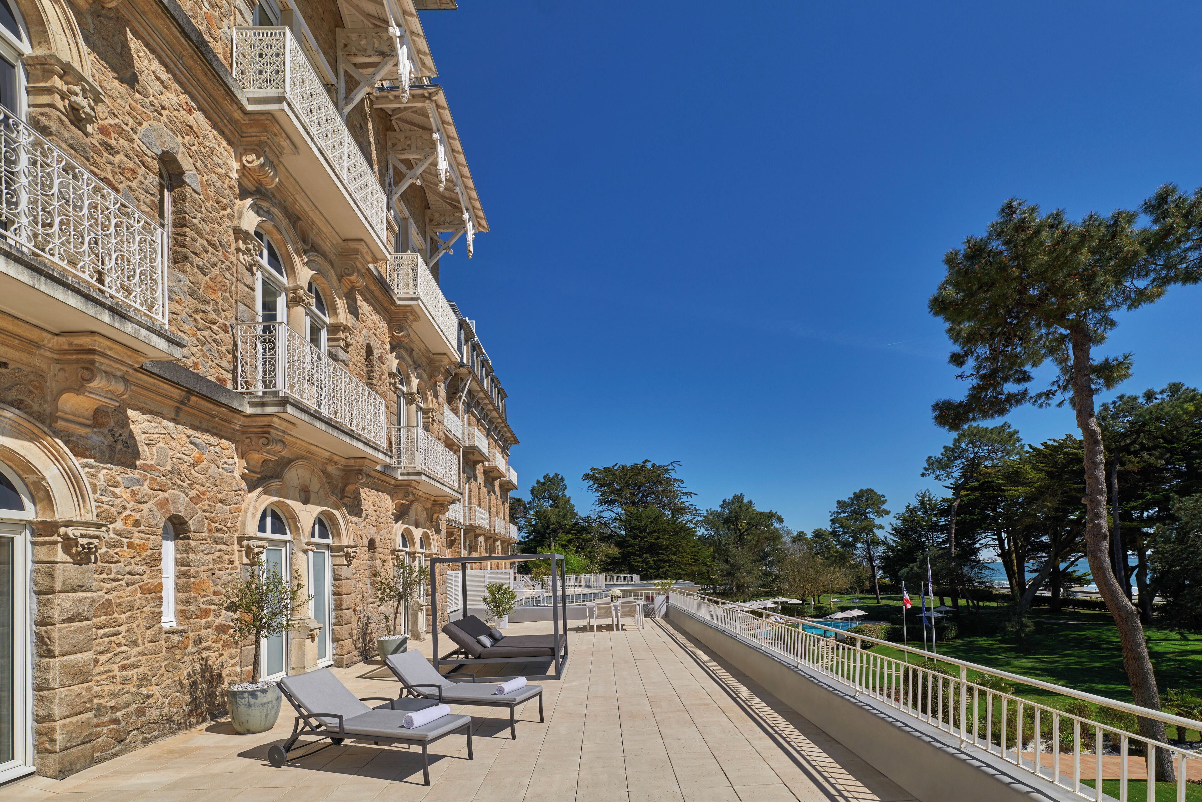 A stone building with a balcony, lounge chairs, and a view of the sea.
