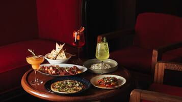 Una mesa de comedor con diversos platos y bebidas, en un ambiente tenuemente iluminado y con asientos tapizados en rojo.