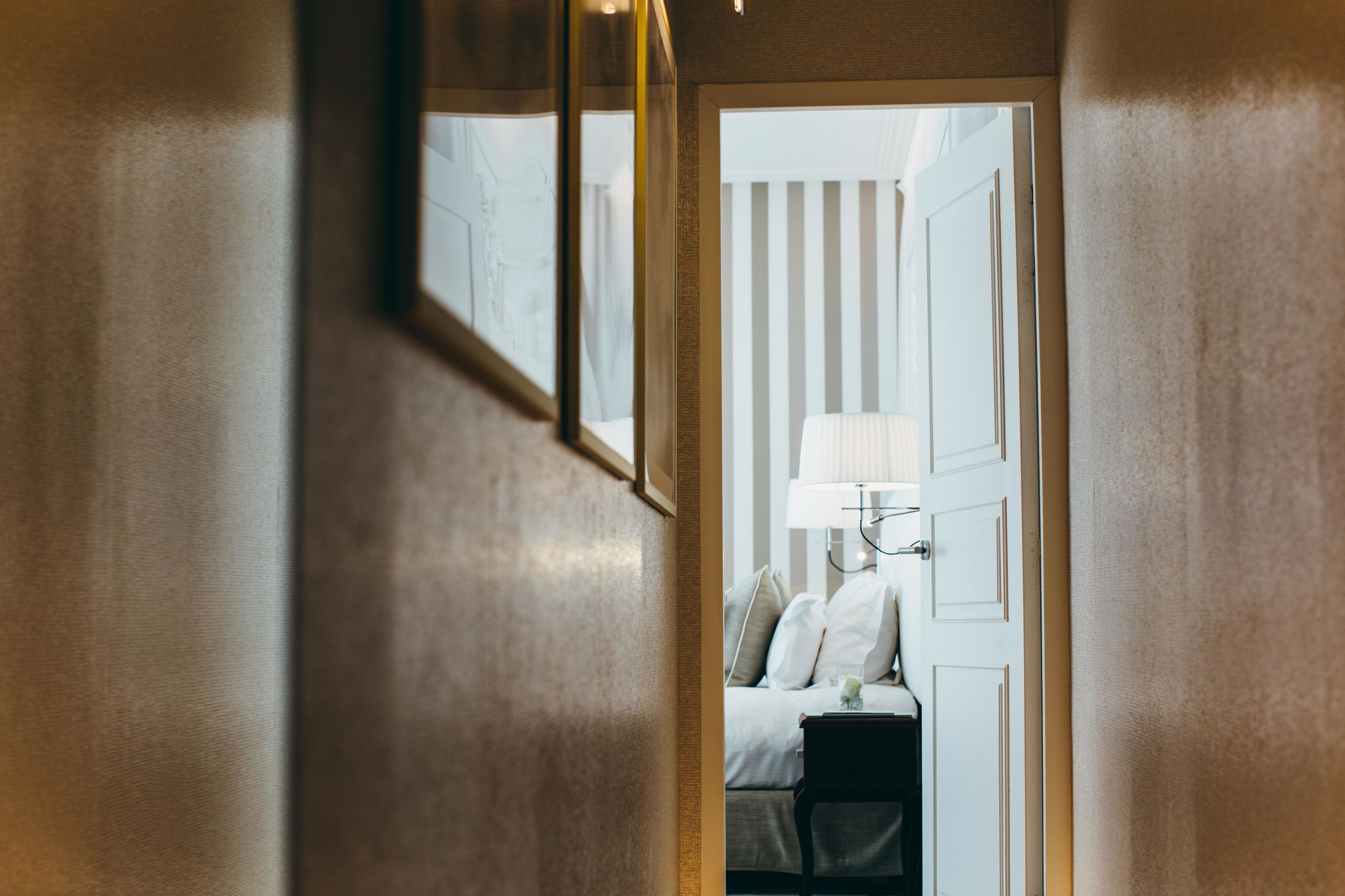 A hallway leading to a bedroom with a bed, a nightstand, and a lamp.