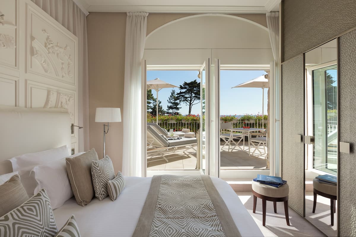 Quarto de hotel com uma cama grande, varanda com mobiliário exterior e vista para o exterior.
