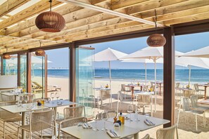 An outdoor dining area with tables and chairs, large umbrellas, and a view of the beach and ocean. - Hôtel Barrière Le Royal La Baule (La Baule-Escoublac)