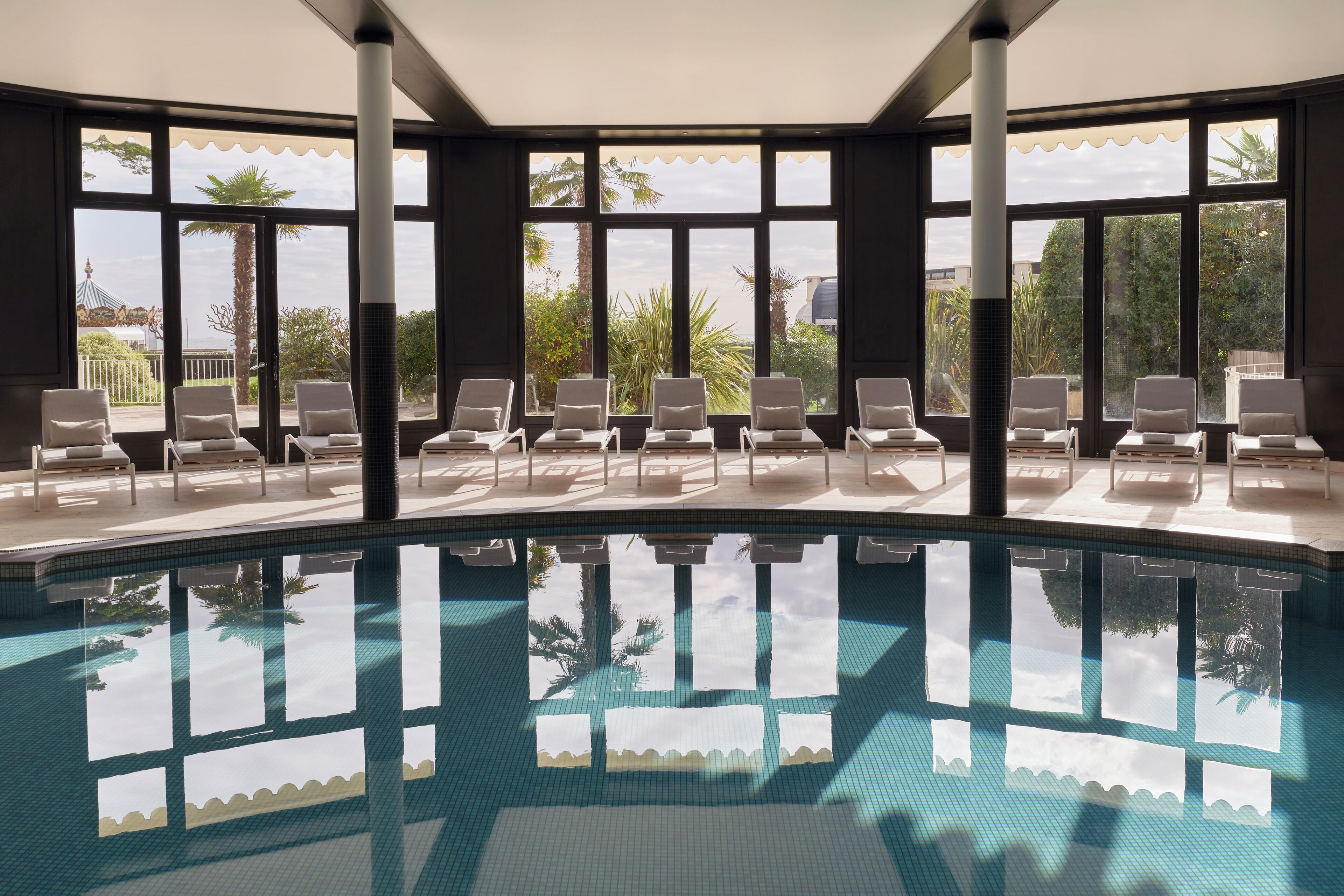 Un área de piscina con sillones reclinables y ventanas amplias.
