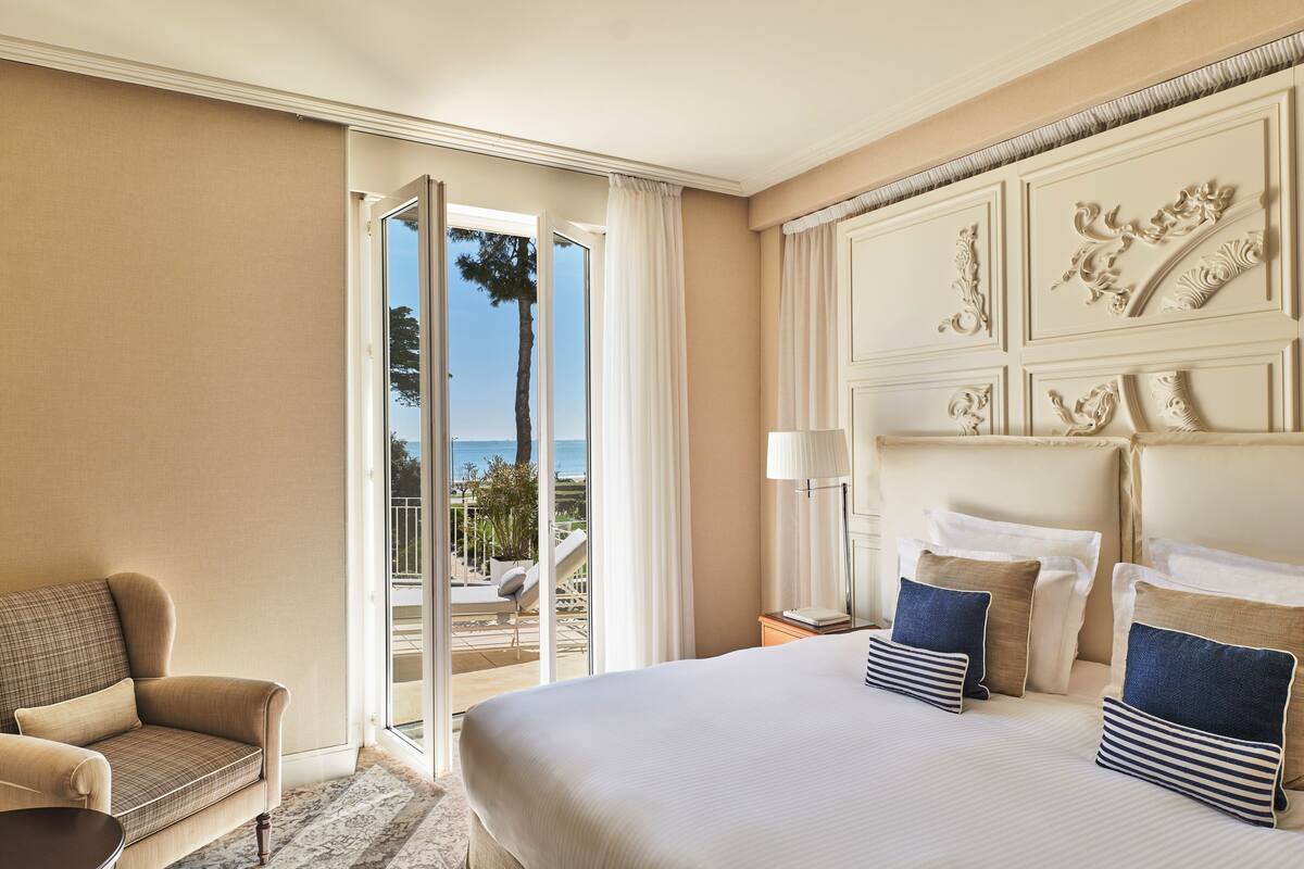 Quarto de hotel com uma cama grande, um sofá, uma mesinha de cabeceira e vista para o exterior.