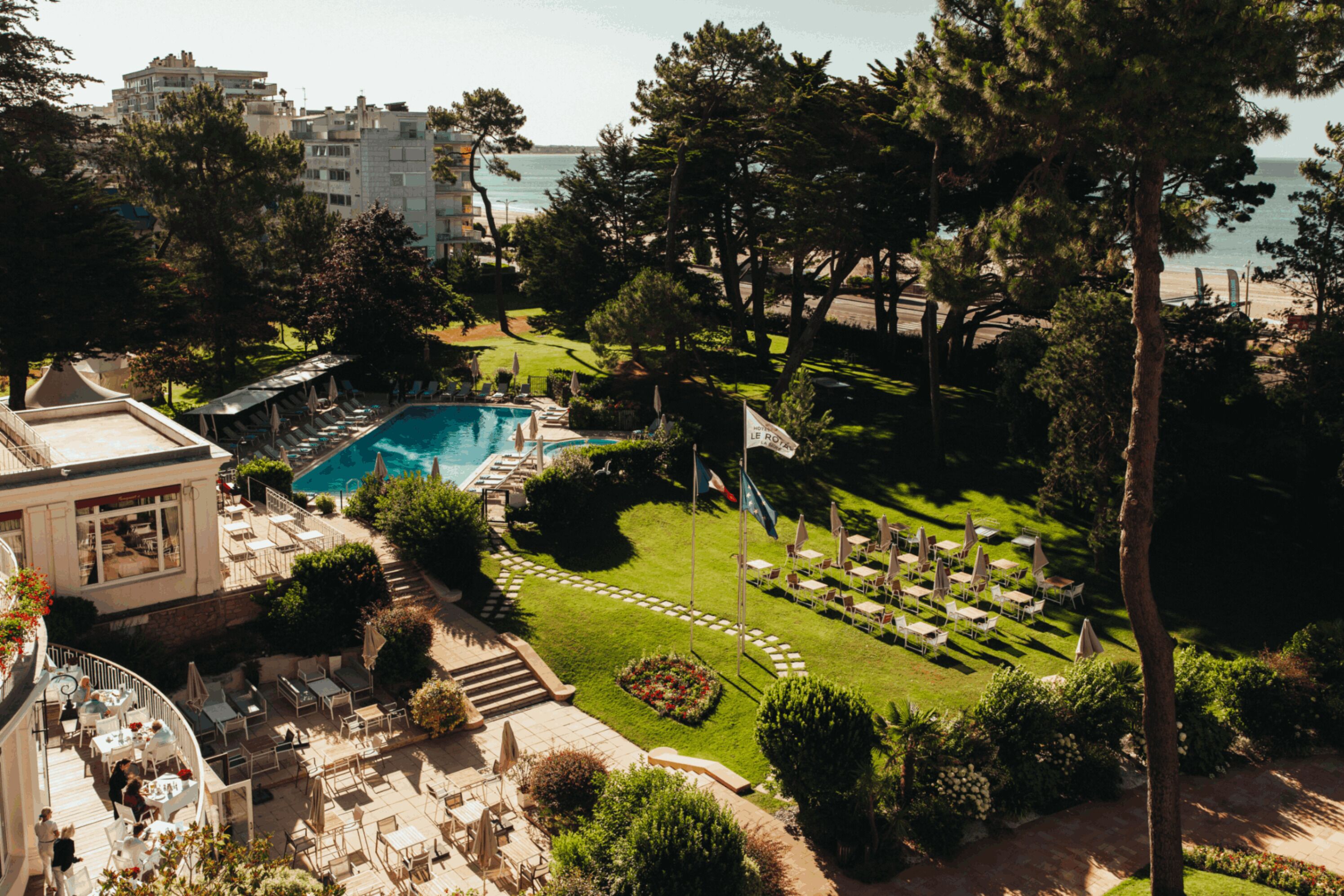 A resort with a swimming pool, outdoor seating, and a view of the sea.