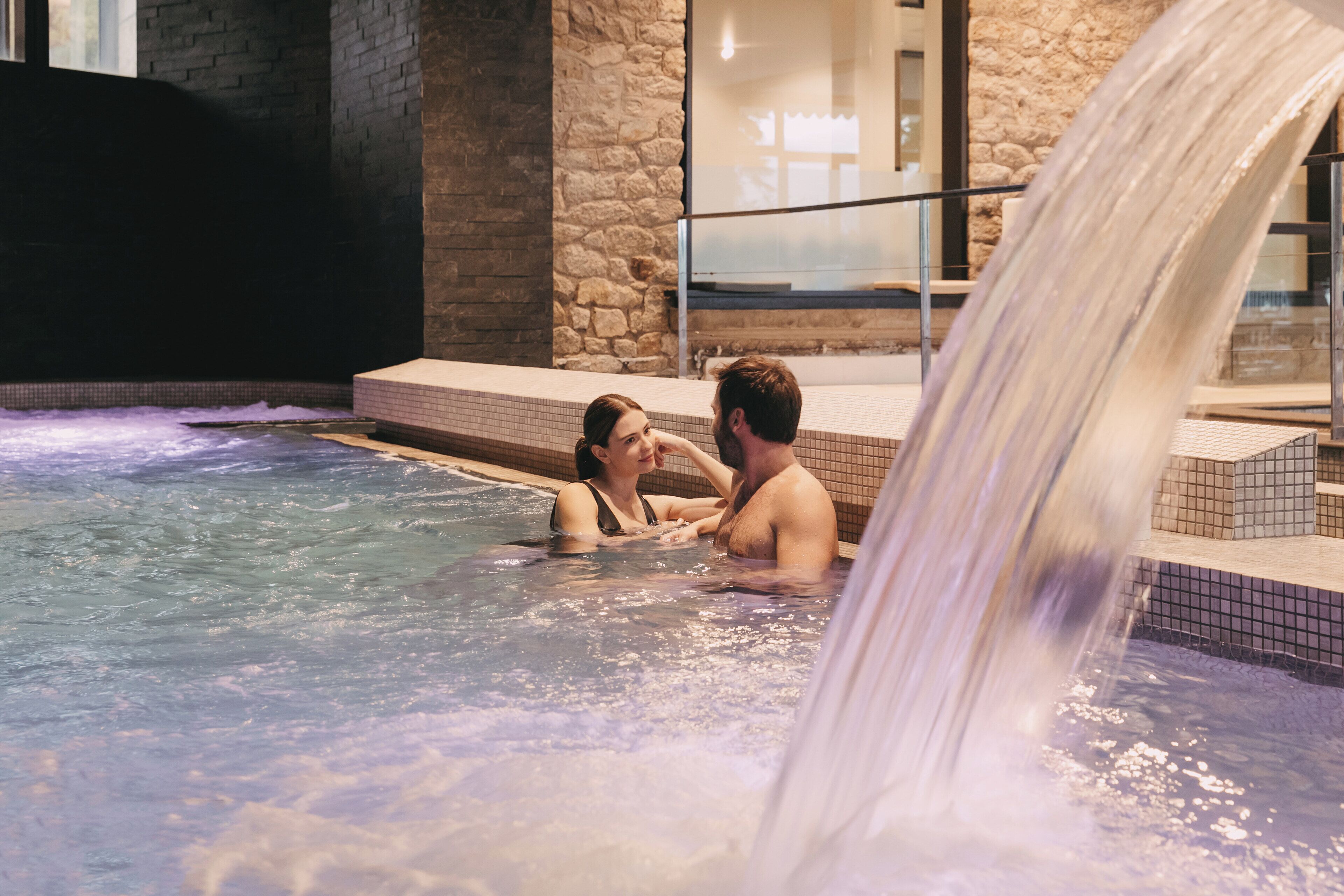 A couple in a hot tub with a waterfall feature.