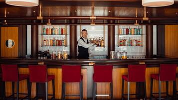 Zona de bar con un cantinero, taburetes rojos y estantes llenos de botellas de licor.