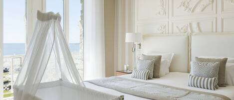 Habitación de hotel con una cama grande, una mesita de noche, una lámpara y vista al mar por la ventana.