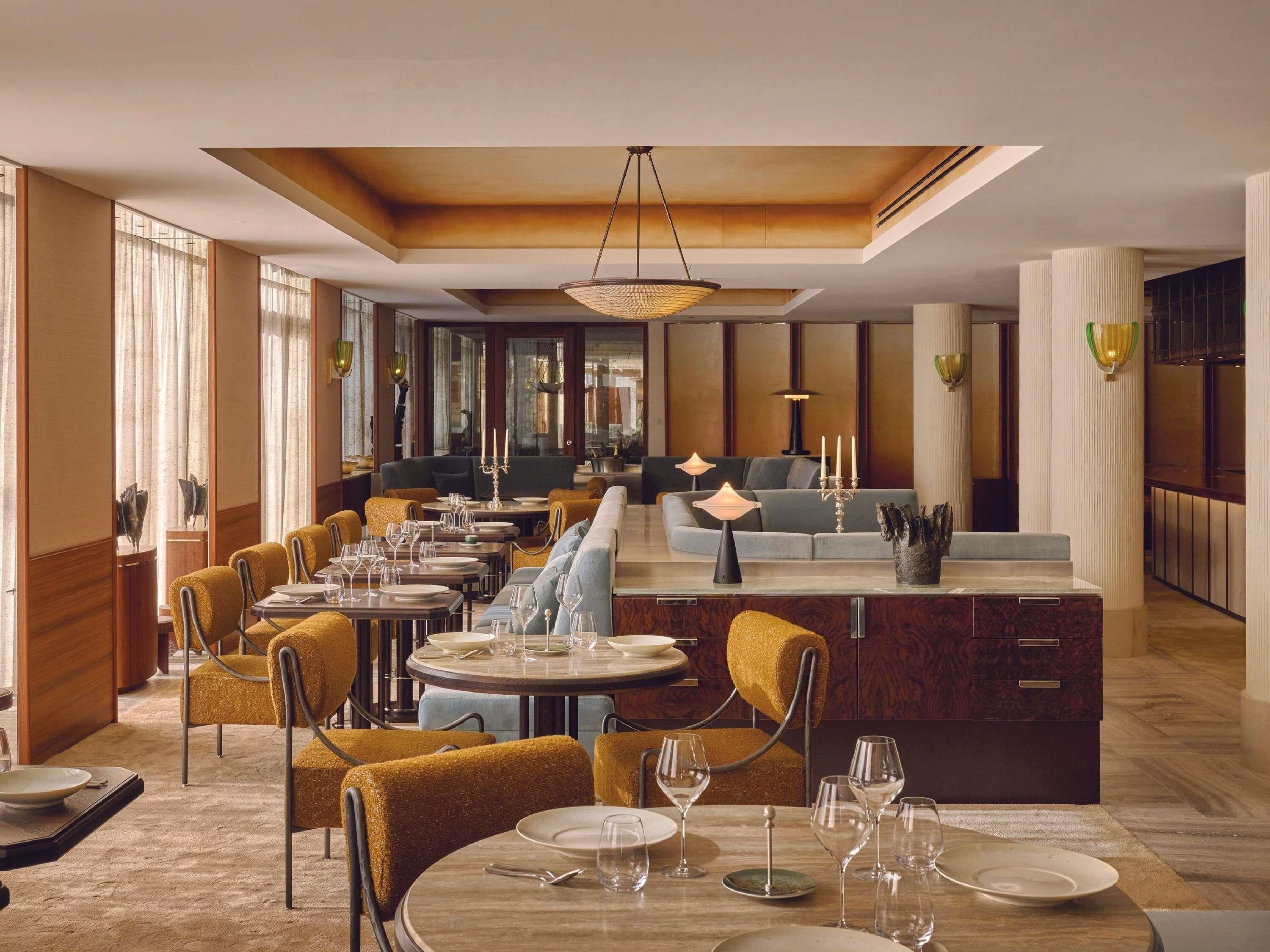 A restaurant with round tables, yellow chairs, and a bar area.