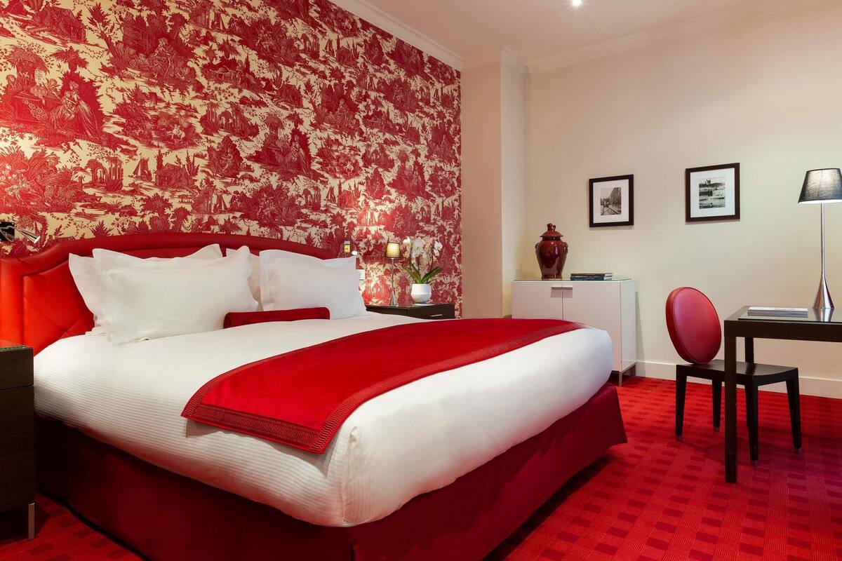 Une chambre d’hôtel avec un grand lit, un bureau, une chaise et une moquette rouge.