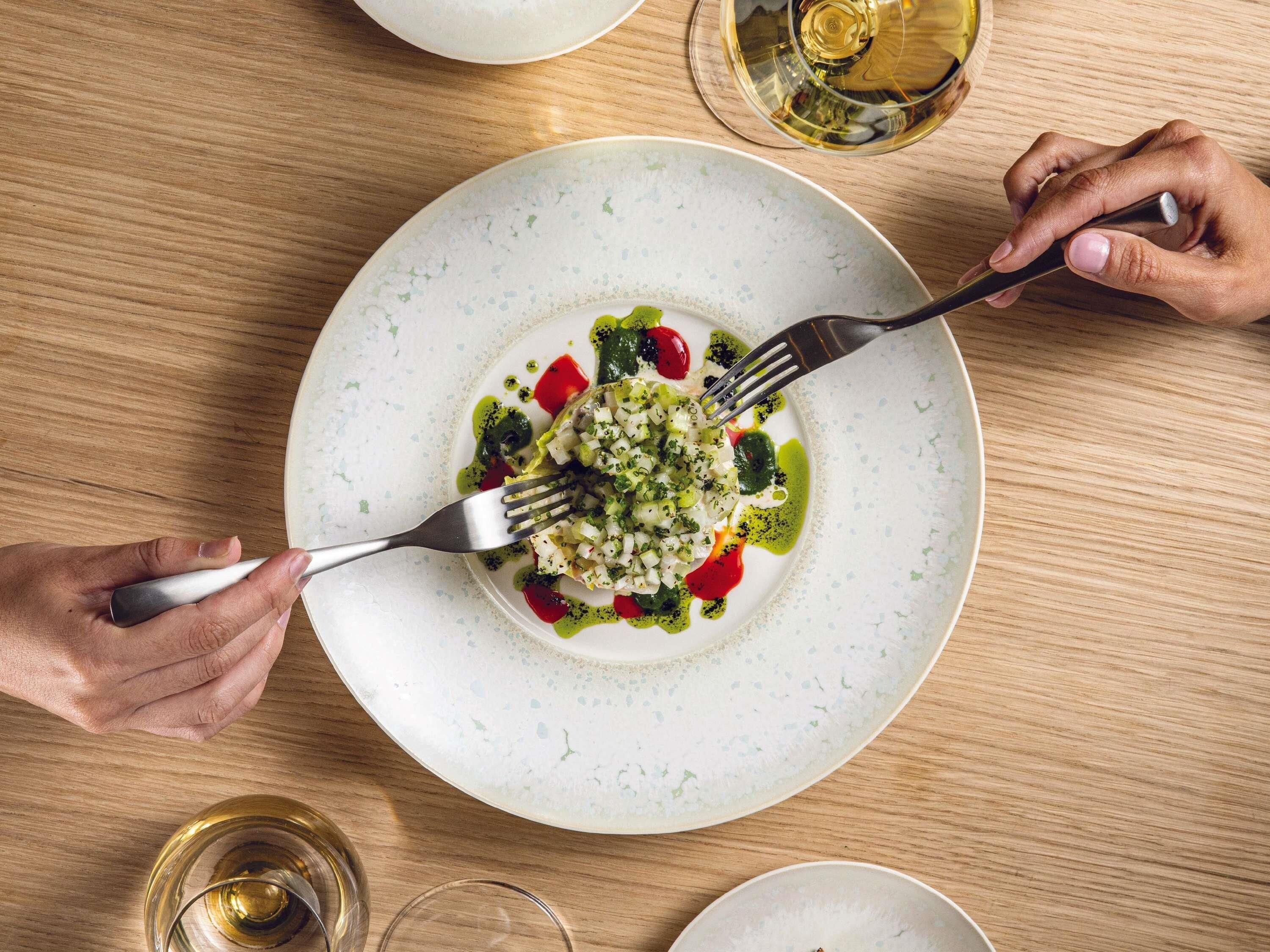 A dining table with a plate of food, a glass of wine, and a fork.